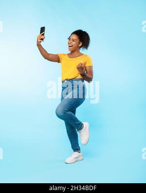 Full length of excited black lady with smartphone making YES gesture, feeling overjoyed, winning online casino bet, shopping on huge discount, achievi Stock Photo