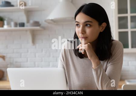 Happy thoughtful Asian student girl sitting at laptop Stock Photo