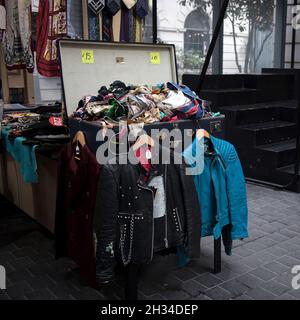 London, UK - 15 September 2021, A blue and black rocker leather jacket hangs on the counter. Box of Silk Scarves for Sale at Spitalfields Antique Mark Stock Photo