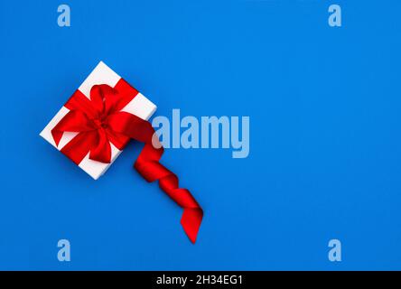 Gift box with red ribbon bow on blue background. Gift card concept Stock Photo