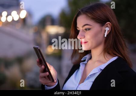Young 20s Caucasian businesswoman reading message on smartphone at evening Stock Photo