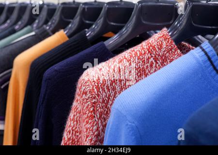 Women's multicolored knitted and crocheted sweaters, jackets hang on hangers in the store Stock Photo