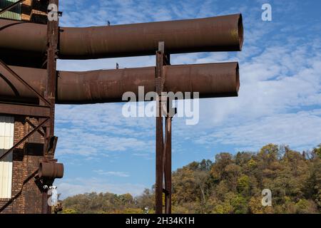 Two large open metal tubes pipes, very rusty, mounted to the side of a warehouse building, blue sky beyond, horizontal aspect Stock Photo