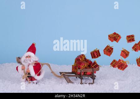 Creative Christmas idea with Santa Claus, snow and sled with lots of gifts in boxes flying in the air. Minimal winter New Year concert. Stock Photo
