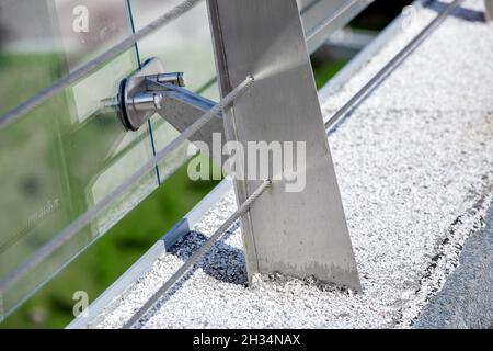 metal turnbuckles fastening of cables with steel rod on pedestrian bridge with stone pebble path and glass barrier for safety close-up details of cons Stock Photo