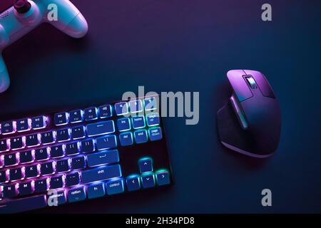 Top down view of color backlighted computer keyboard, mouse and game controller on desk. Professional computer game playing, esport business and onlin Stock Photo