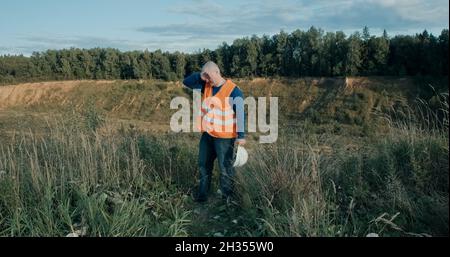 Working engineer in a white helmet next to a sand pit. The man is very tired Stock Photo