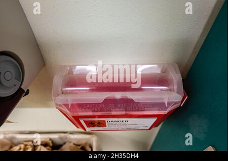 Red biohazard sharps waste container mounted to the wall of a public restroom Stock Photo