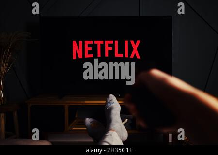 Online streaming service. Boy hold remote control in hand and TV set with NETFLIX service logo. Katy Wroclawskie, Poland - October 25, 2021 Stock Photo