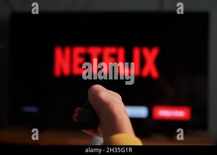 Online streaming service. Boy hold remote control in hand and TV set with NETFLIX service logo. Katy Wroclawskie, Poland - October 25, 2021 Stock Photo
