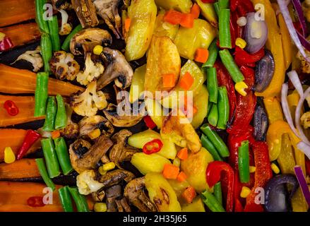 Baked potatoes, carrots, green beans, champignon, mushrooms, cauliflower, paprika, onion in a roasting pan. Vegetarian food background. Stock Photo