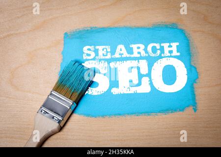 Search, SEO concept. Blue paint and paint brush on a wooden surface. Stock Photo