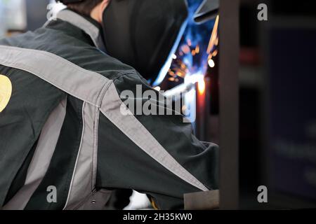 Industrial welder in a helmet is welding metal plates. Selective focus. Stock Photo