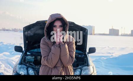 Frozen woman in warm jacket stands near broken automobile Stock Photo