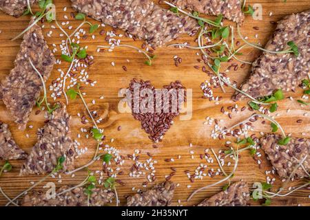 Crispy seed homemade bread decorated with microgreen sprouts with a heart shaped figure laid out from flax seeds on a wooden table. Healthy snack. Fla Stock Photo