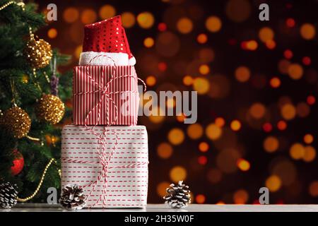Christmas gift boxes with santa hat under the Christmas tree on a blurry background of garland lights. Stock Photo