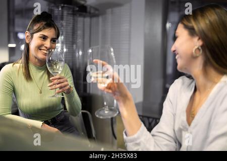 Happy women best friends drinking white wine at bar restaurant counter- Female friendship concept with young girlfriends enjoying time and having genu Stock Photo
