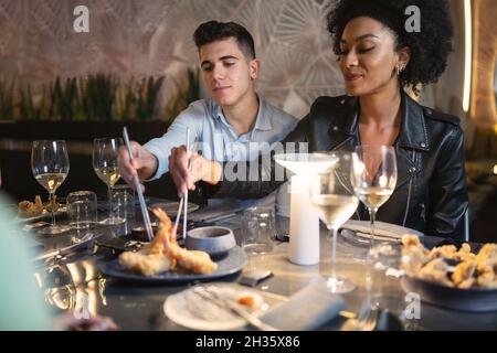 Multi cultural young couple taking seafood at the fusion food restaurant with metal chopsticks - concept of young people eating together international Stock Photo
