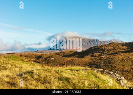 Quinag mountain range in Assynt, Sutherland, Scottish Highlands in Autumn with burnished orange moorland and clear blue sky.  Low lying cloud formatio Stock Photo