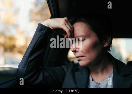 Businesswoman with severe headache sitting at the backseat of a car, selective focus Stock Photo