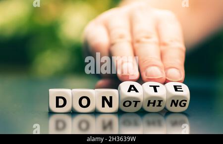 Hand turns dice and changes the expression "do nothing" to "donate". Stock Photo