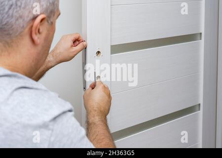 a man fixing a door lock at home using a screwdriver Stock Photo
