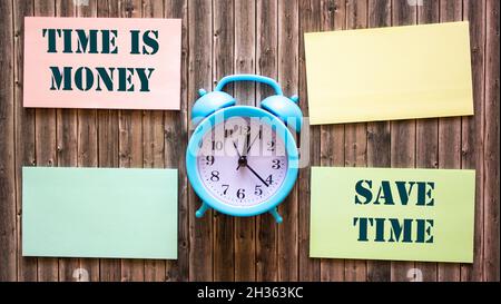 On a wooden background, an alarm clock and multi-colored stickers with the inscription time is money and saving time Stock Photo