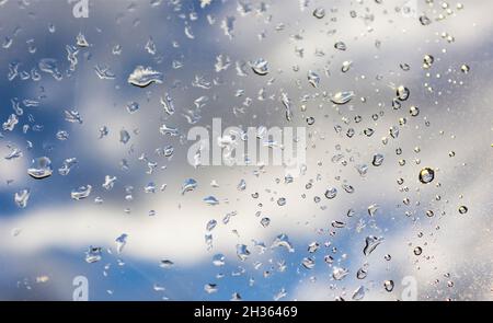 Raindrops on the window pane, blue sky and clouds visible through the transparent glass of the window Stock Photo