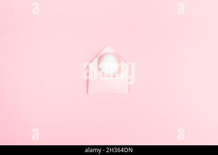 Easter festive minimal concept with one white egg on envelope on pastel pink. Holiday creative trendy monochrome background. Easter congratulation con Stock Photo