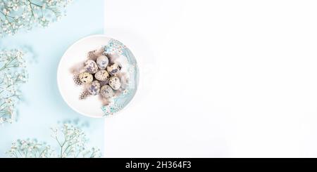 Easter table setting concept with quail eggs on plate with white flowers on pastel white and light blue backdrop. Easter festive banner. Passover mini Stock Photo