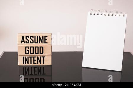 Assume good intent. Inspirational quote on wooden blocks with notepad to write on white and black background. Positivity concept Stock Photo