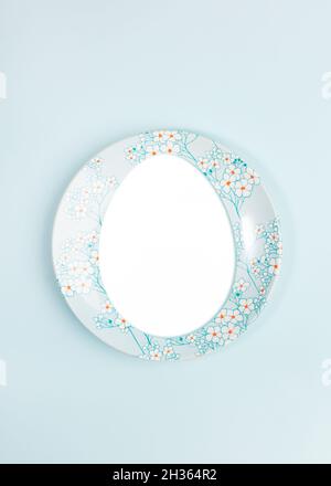 Easter creative festive minimal composition with copy space in egg shape on beautiful plate on center of light blue backdrop. Holiday layout. View fro Stock Photo