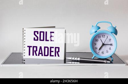 SOLE TRADER, text on white notepad on black and white background with clock and pen Stock Photo