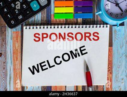 WELCOME SPONSORS word written on notepad with alarm clock, calculator, stickers against a wooden table. Stock Photo