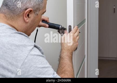 a man fixing a door lock at home using a portable screwdriver Stock Photo