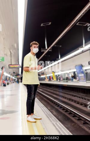 Young man wearing a face mask holding a cell phone in a subway station Stock Photo