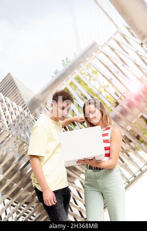Young student couple looking at a laptop computer outside next to a modern sculpture Stock Photo