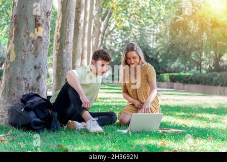 Two young college students sitting on the campus lawn studying with a laptop computer Stock Photo