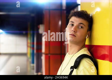 Young man listening to music leaning against the wall and looking aside Stock Photo