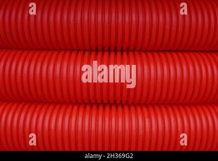 Red plastic corrugated tubing, synthetic pipes used in construction, as abstract view, background. Selective focus on middle part of picture. Stock Photo