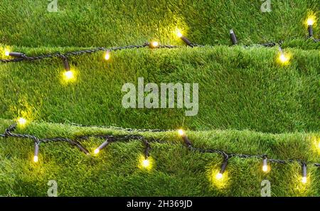 Unusual Christmas Tree background made from artificial grass decorated with golden garlands. Selective focus. Stock Photo