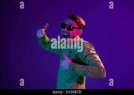 Photo portrait of smiling man wearing sunglass showing thumb-up sign smiling cheerful isolated on dark purple color background Stock Photo
