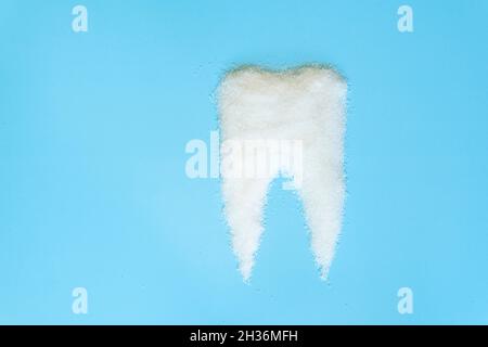 the concept of the harmful effect of sugar on tooth enamel. Sugar is laid out of granulated sugar on a blue background. medical concept Stock Photo