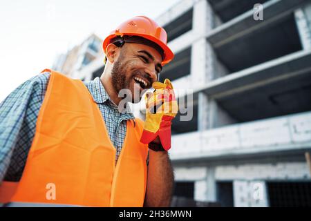 Young construction worker in uniform using walkie talkie on site Stock Photo