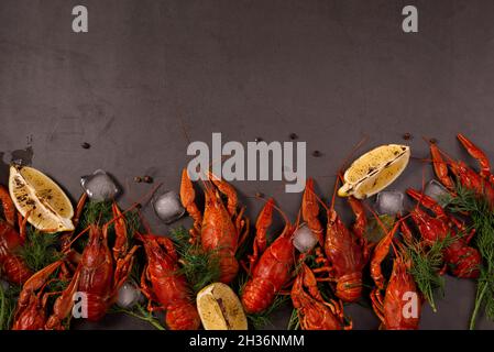 Boiled red crawfish, ready to eat with lemon slices and ice cubes on a black surface. Stock Photo