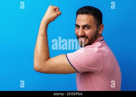 Hispanic man with beard wearing casual t-shirt showing arms muscles against blue background Stock Photo