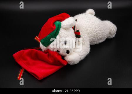 White Christmas bear toy with red dwarf hat and red gift bag isolated on black background Stock Photo