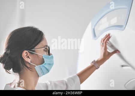 woman radiologist doctor adjusting computer tomography scanner machine to make CT test. female technician with face mask on working in a hospital or c Stock Photo