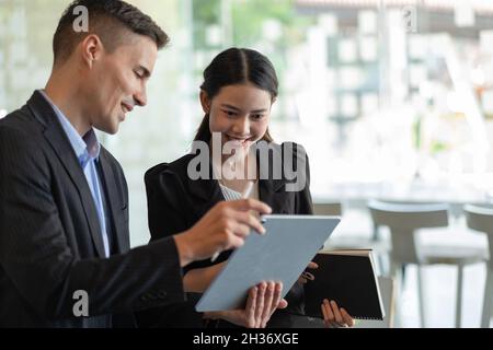 Focused diverse ethnicity coworkers team brainstorming on digital tablet,asian and caucasian business colleagues share ideas sit at work desk looking Stock Photo