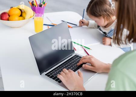 Woman using laptop near daughter with down syndrome drawing in kitchen Stock Photo
